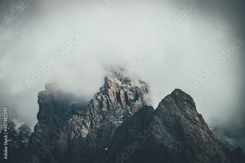 Photography Dark atmospheric surreal landscape with dark rocky mountain top in low clouds in gray cloudy sky