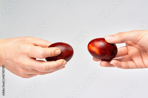 Two hands holding Easter eggs check their strength on a light background
