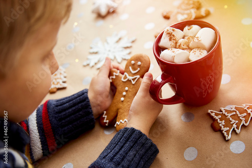 Child holds Christmas homemade gingerbread cookie near hot drink and marsmallows. Cozy home Christmas atmosphere and warmth concept. Festive table setting photo