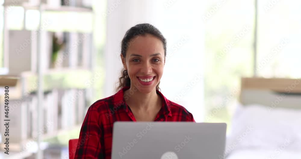 Cheerful ethnic woman in casual clothes closing laptop and taking mug of hot beverage while sitting at desk and working on remote project at home Cheerful ethnic woman in casual clothes closing laptop and taking mug of hot beverage while sitting at desk and working on remote project at home