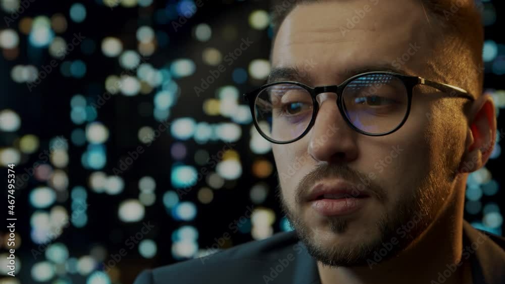 Close-up portrait of a young man working at the computer. Laptop display is reflected in glasses. Night city lights on the background. Business, coding and exchange concept. Close-up portrait of a young man working at the computer. Laptop display is reflected in glasses. Night city lights on the background. Business, coding and exchange concept.