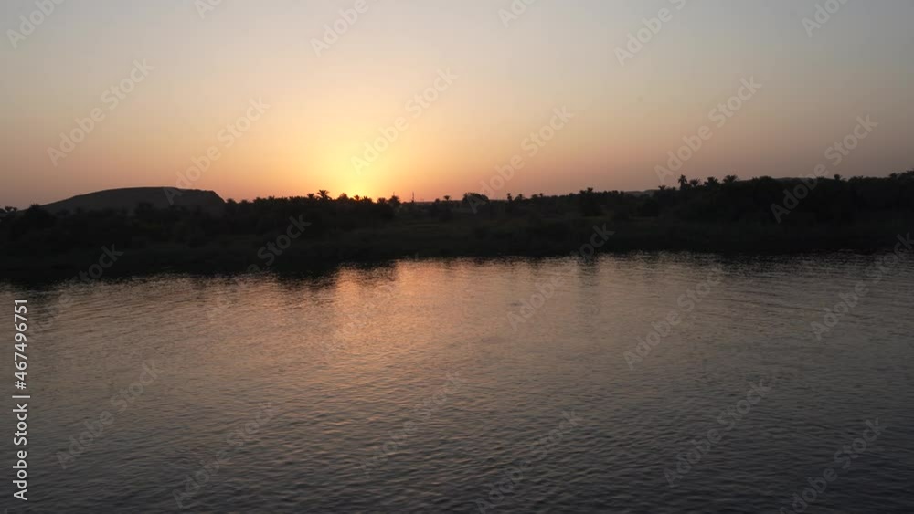 Evening twilight. The Nile River flows calmly . The setting sun rolls over the hills and trees. The sky is highlighted in orange. Egypt Evening twilight. The Nile River flows calmly . The setting sun rolls over the hills and trees. The sky is highlighted in orange. Egypt