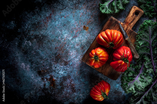 Flat lay of big fresh ripe tomatoes with kale leaves and wooden cutting board on the rustic dark blue background photo