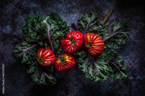 Flat lay of big fresh ripe tomatoes with kale leaves and wooden cutting board on the rustic dark blue background photo