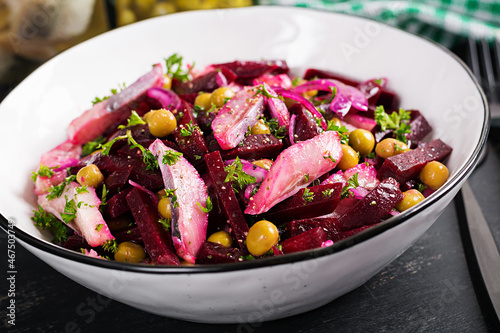 Salad with herring, green peas and beetroot filled with vegetable oil on a dark table.