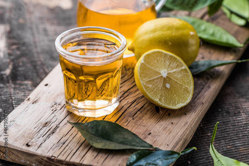 Traditional homemade lemon liqueur limoncello and fresh citrus on a wooden table.