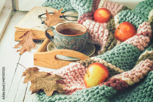 A сup of tea, a book, dry leaves and apples on the wooden windowsill. Autumn concept. 