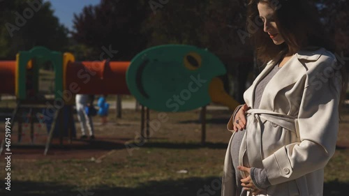 4K footage of a pregnant girl near the playground strolls in the park and imagines her baby with her
