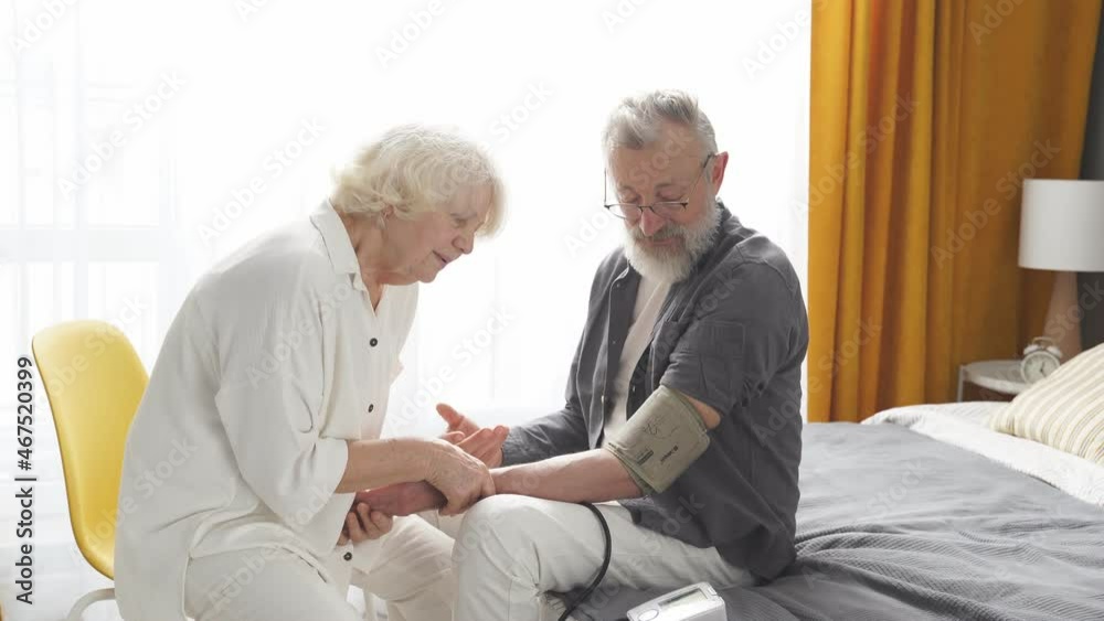 Mature woman controlling blood pressure of husband using tonometer. Concept of home health check, medicine, healthcare. Mature woman controlling blood pressure of husband using tonometer. Concept of home health check, medicine, healthcare.