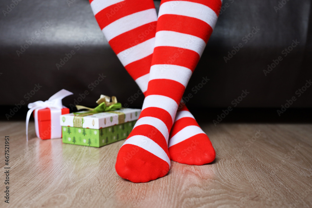 Female legs in Christmas knee socks on a floor near the gift boxes. Woman sitting on a bed in home, New Year celebration Female legs in Christmas knee socks on a floor near the gift boxes. Woman sitting on a bed in home, New Year celebration