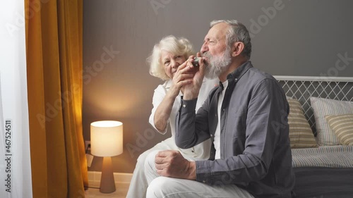 Senior man using asthma inhaler for relief an attack at home for preventing attack, wife support.