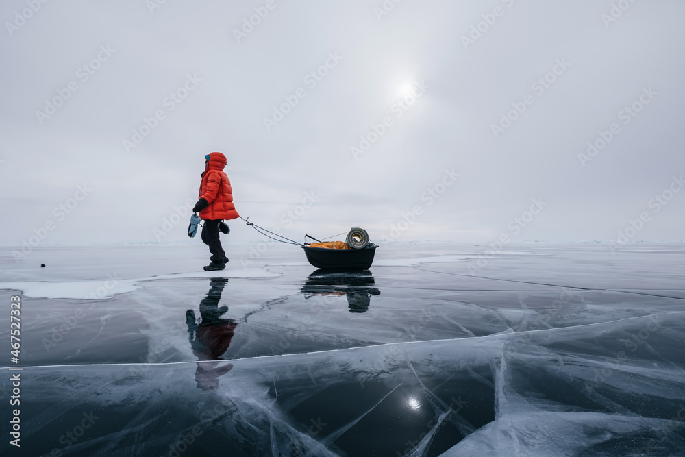 Naklejka premium Tourist walking with sleigh dragging on the frozen ice of Lake Baikal. Winter trekking