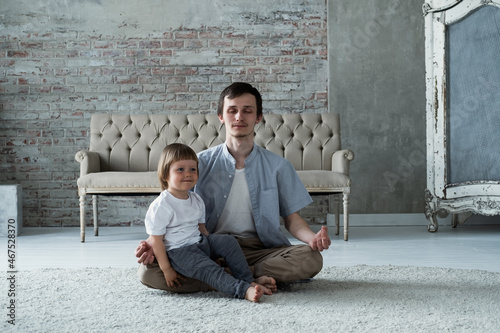 Young father trying to meditate sitting in lotus yoga pose with little son kid © Annatamila