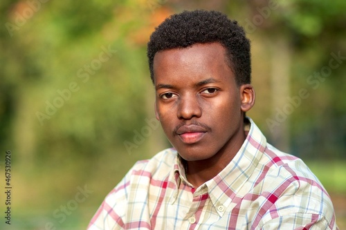 Close up portrait of sad serious pensive thoughtful nice guy, young handsome black African Afro American ethnic man in shirt looking at camera outdoors in park on natural background.