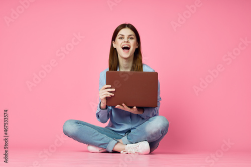 woman sitting on floor with laptop shopping entertainment pink background