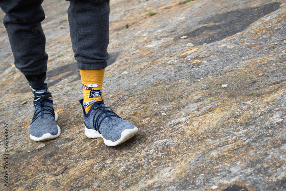 Legs of man in tracksuit walking on rock among dinosaur footprints. Socks of different colors, summer slippers. Legs of man in tracksuit walking on rock among dinosaur footprints. Socks of different colors, summer slippers.