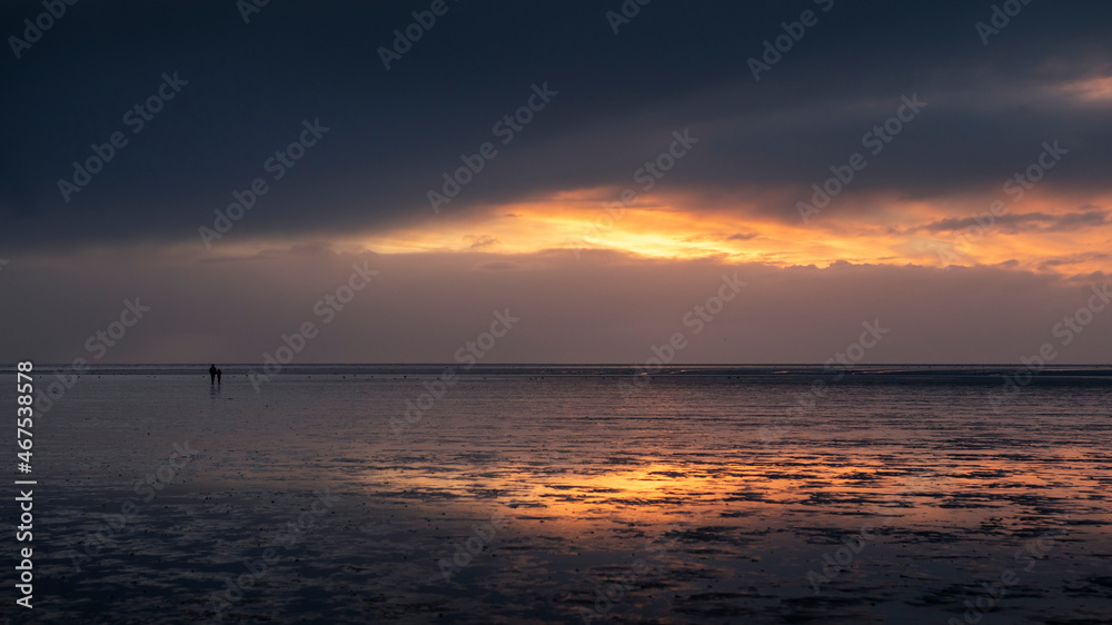 Couple silhouette walking along the Wadden Sea in Buesum during sunset, reflecting in the wet sand, Germany. Couple silhouette walking along the Wadden Sea in Buesum during sunset, reflecting in the wet sand, Germany.