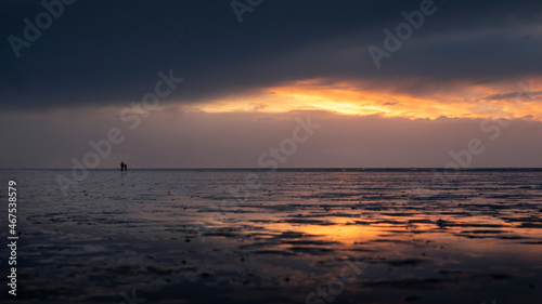 Couple silhouette walking along the Wadden Sea in Buesum during sunset, reflecting in the wet sand, Germany.