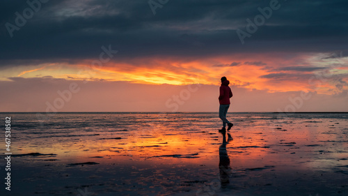 Woman silhouette walking along the Wadden Sea in Buesum during sunset  reflecting in the wet sand  Germany.