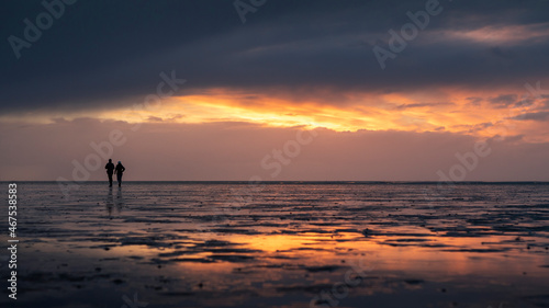 Couple silhouette walking along the Wadden Sea in Buesum during sunset, reflecting in the wet sand, Germany. © Bastian Linder