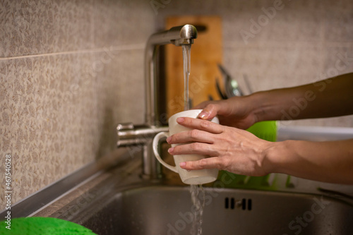 Woman's hands washing white cup in the sink. Housework in the kitchen concept. Dishwasher