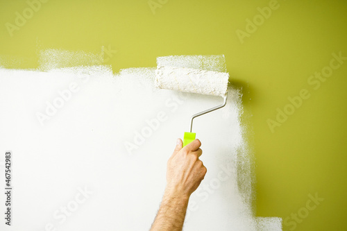Male decorator painting wall with roller indoors. Painting work.