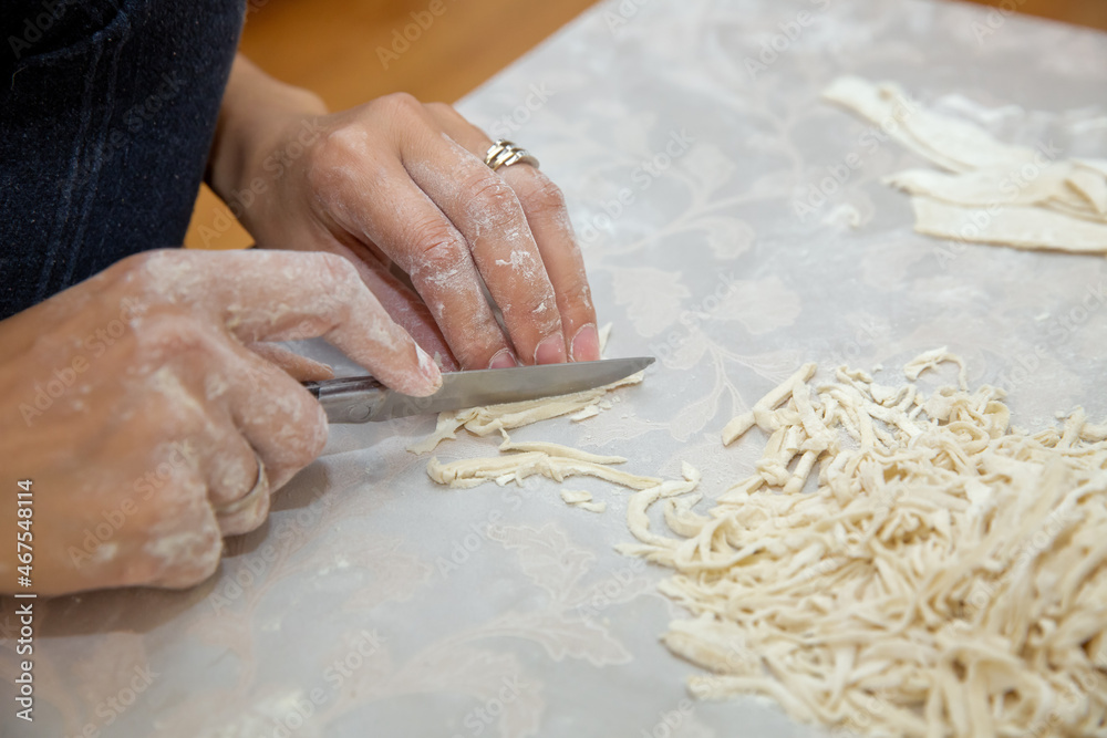 Cutting long dough stripe for cooking pasta. Homemade food preparation concept. Closeup of process of making cooking homemade pasta. Erishte . Young house wife preparing the homemade pasta at kitchen.