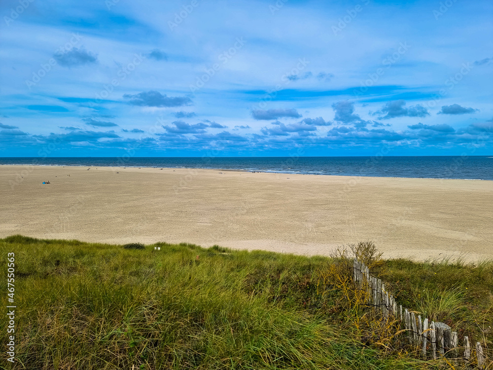Panorama view of Dunes with marram gras and an empty beach on the Dutch island of Texel on a  with a blue cloudy sky in summer. Tourism and vacations concept. National park Duinen van Texel