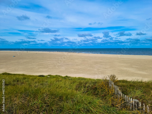 Panorama view of Dunes with marram gras and an empty beach on the Dutch island of Texel on a with a blue cloudy sky in summer. Tourism and vacations concept. National park Duinen van Texel