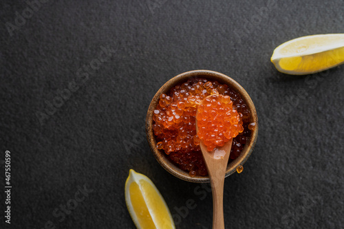  fresh red caviar with a wooden spoon on a dark background, in a ceramic bowl. copyspace