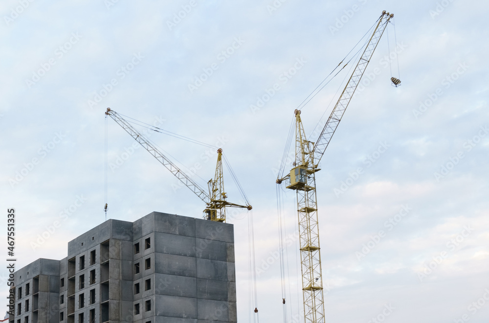 Against the background of the sky, there is a multi-storey building under construction and two cranes Against the background of the sky, there is a multi-storey building under construction and two cranes