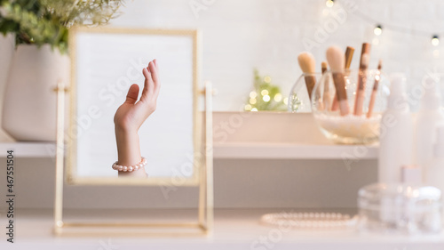 Reflection in table mirror of woman hand  in pearl bracelets on dressing table with make up accessories. Self-Care.