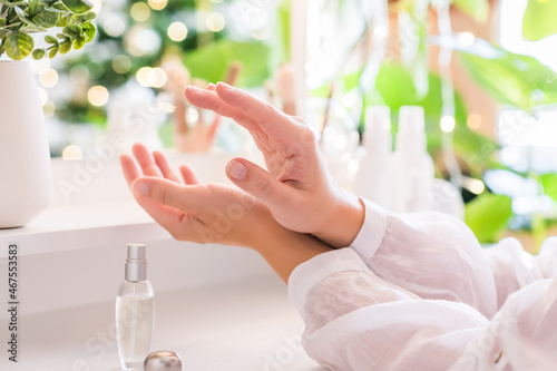 Woman applying perfume on her hand sitting near dressing table with make up accessories and table mirror. Self-Care.