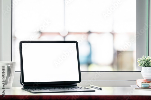blank white screen tablet with magic keyboard on wooden table.