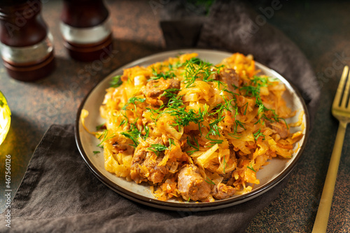 Braised cabbage. Stewed cabbage or bigos with turkey meat in a ceramic plate on a dark background. Traditional Polish dish 