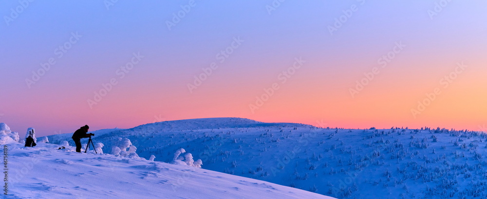 Photographer taking a photo in winter mountain landscape at sunrise. - obrazy, fototapety, plakaty 