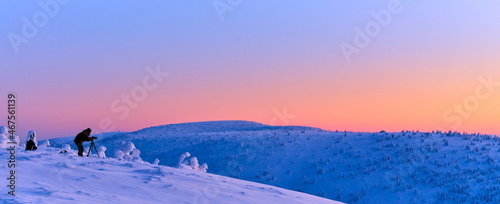 Photographer taking a photo in winter mountain landscape at sunrise.