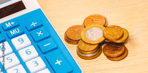 Dinheiro, Brasil. Moedas do Real Brasileiro - BRL, sobre uma mesa de madeira ao lado de uma calculadora azul. Pouco dinheiro, inflação e crise financeira. photo