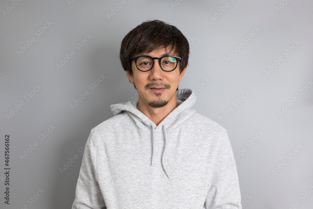 Fototapeta premium Adult asian man in grey sweater and eyeglasses smiling on a grey background.