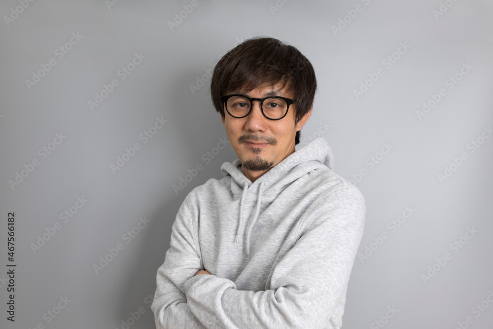 Adult asian man in grey sweater and eyeglasses smiling on a grey background.