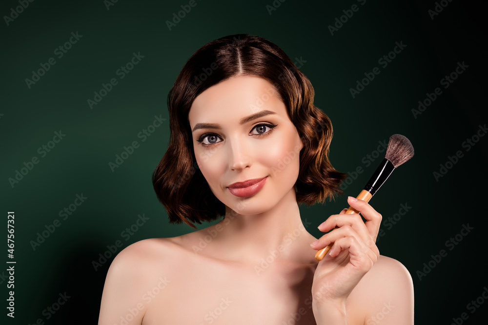 Obraz premium Portrait of smiling cool professional makeup artist girl with naked shoulders hold big brush isolated on green color background