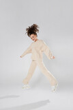 Inspired positive young woman in sneakers and fashion sportswear jumps on white background. Gorgeous young female model with dark wavy hair jumping in the studio. Not isolated with copy space