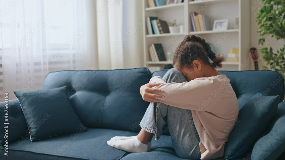 Upset teenage girl sitting on the sofa at home, feeling lonely, family problem Upset teenage girl sitting on the sofa at home, feeling lonely, family problem