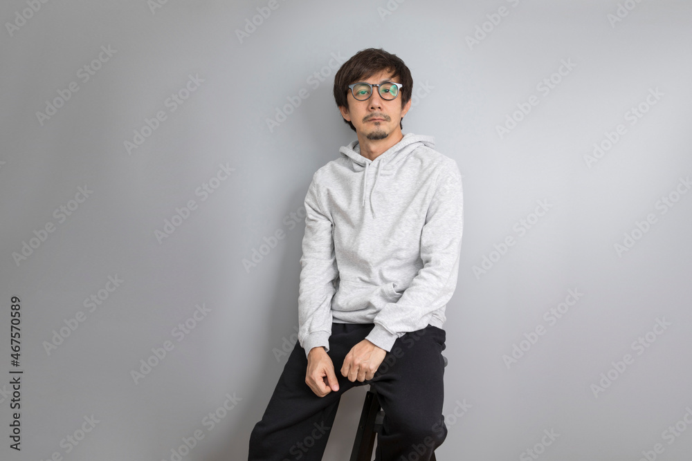 Chill and relax asian man in white hoodie sitting on a stool on grey background. Chill and relax asian man in white hoodie sitting on a stool on grey background.