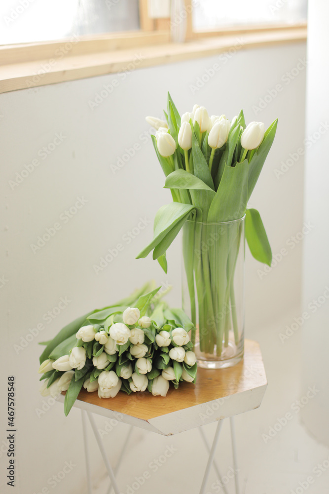 Obraz premium Bouquet of white tulips in glass vase on wooden table. Fresh flower for the gift. Bridal bouquet.