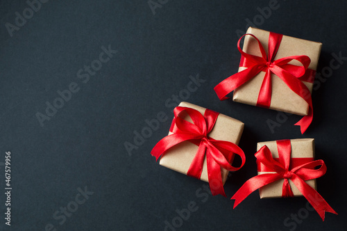 Fototapeta Naklejka Na Ścianę i Meble -  Festive concept - gifts with craft paper with a red bow on a black background. composition for christmas, new year and holidays. flat lay with place for text.
