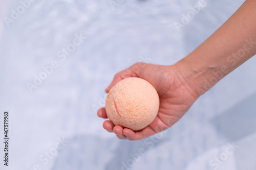 Beautiful woman holding an aromatic orange bath bomb on her hands before put it into the bathtub.