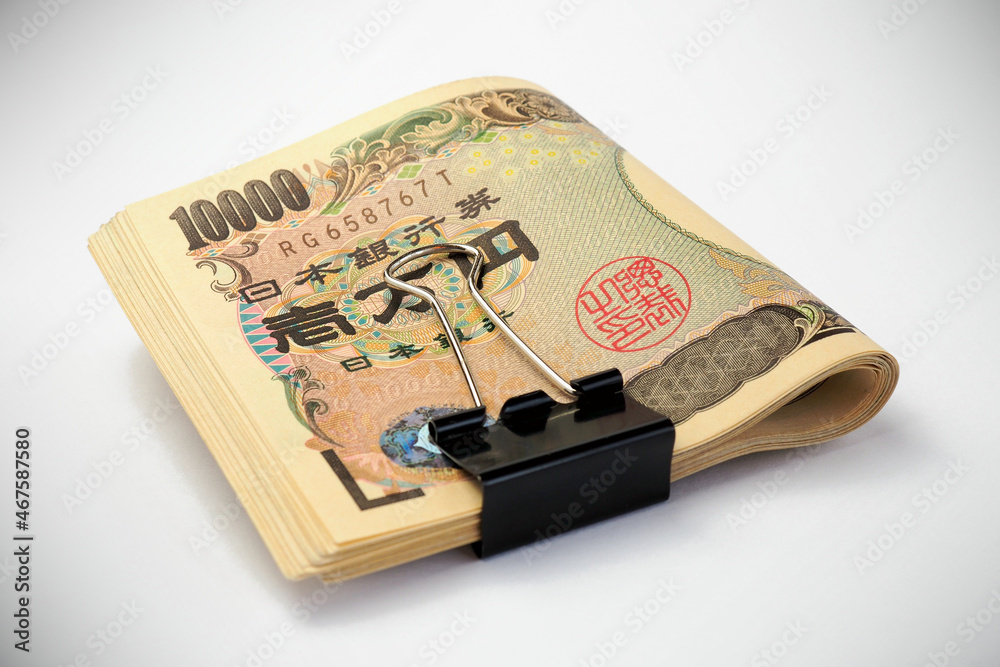 A rolled up bundle of Japanese bills of 10,000 yen. Money tied with a binder clip and lie on a white surface. Banking, finance and the economy of Japan. Illustration with vignetting. Macro A rolled up bundle of Japanese bills of 10,000 yen. Money tied with a binder clip and lie on a white surface. Banking, finance and the economy of Japan. Illustration with vignetting. Macro
