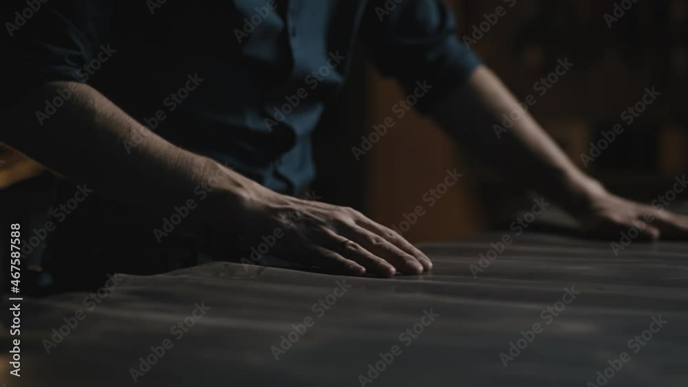 Tracking shot of unrecognizable man tailor rolling out piece of leather before making garment, close up