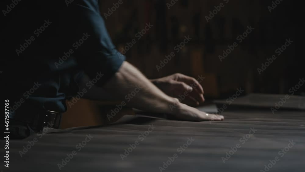 Tailor workshop. Close up of unrecognizable male craftsman rolling out and smoothing piece of leather on table